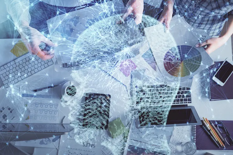 Cyfrowa sieć w kształcie ludzkiej głowy nałożona na widok biurka z dokumentami i laptopami – symbolika cyfrowej transformacji biznesu i integracji AI.