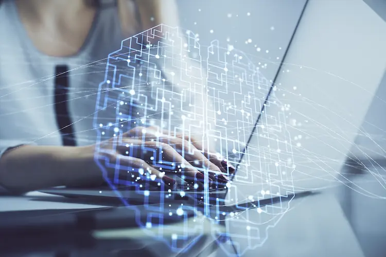 Cyfrowy, świecący mózg z obwodami nałożony na dłonie piszące na laptopie – symbol cyfryzacji firm i wdrażania AI w biznesie.