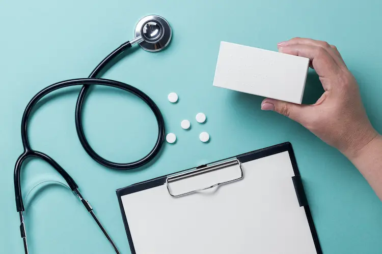 Stetoskop lekarski, podkładka na dokumenty i dłoń trzymająca opakowanie leków – wizualizacja gwarancji dostępności usług medycznych w Enel-med.