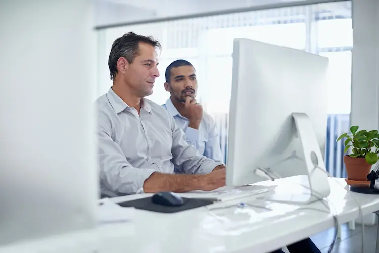 Specjaliści IT współpracujący przy biurku podczas tworzenia aplikacji w technologii low-code przed monitorem komputera.