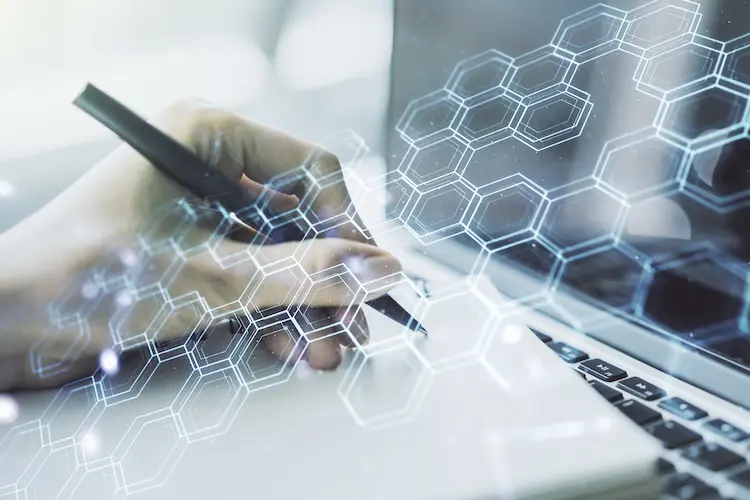 Dotacje na cyfryzację firmy – dłoń pisząca przy laptopie z nałożoną grafiką cyfrowych heksagonów symbolizujących innowacje.