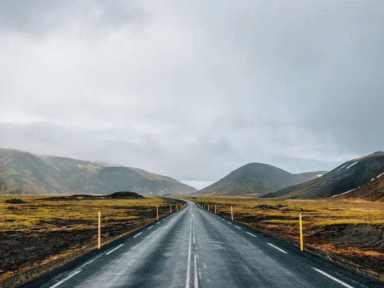 Długa, pusta droga asfaltowa biegnąca przez surowy górzysty krajobraz – symbolika mobilności i samochodów kompaktowych w firmie.