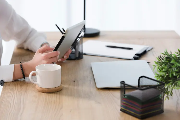 Osoba przeglądająca oferty nieruchomości na tablecie przy biurku z kawą – analiza obecności Polaków na globalnym rynku nieruchomości.