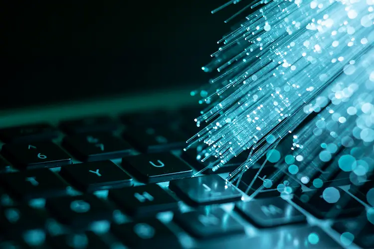 Zbliżenie na klawiaturę laptopa z wiązką świecących światłowodów – wizualna metafora transformacji cyfrowej i nowoczesnych technologii.