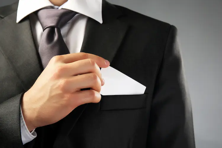Zbliżenie na biznesmena w garniturze wkładającego białą kartę do kieszeni – symbolika ultralidera i przywództwa przyszłości.