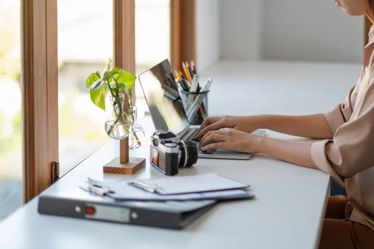 Kobieta pracująca na laptopie w jasnym biurze przy oknie – analiza jak wskaźnik WIBOR wpływa na raty kredytów.