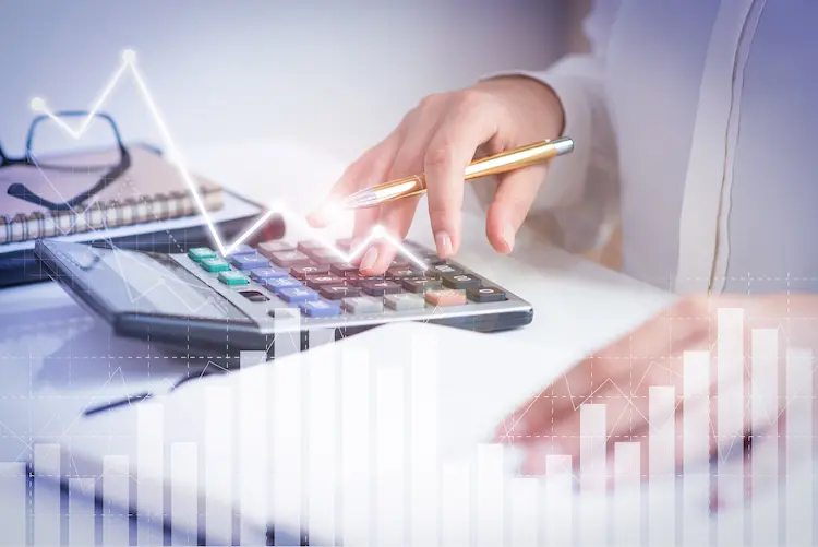 Dłonie osoby używającej kalkulatora z wykresami finansowymi i strzałką wzrostu w tle