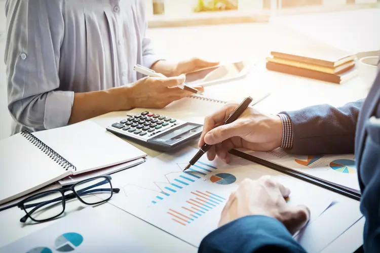 Spotkanie biznesowe - analiza wykresów finansowych i dokumentów z kalkulatorem na stole