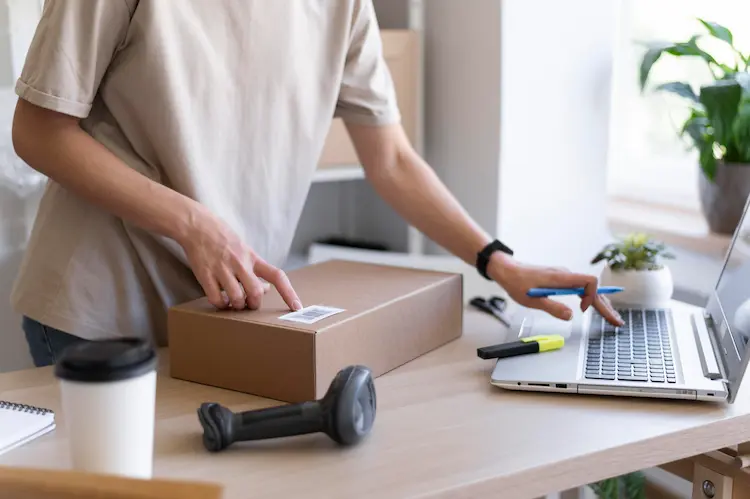 Kobieta pakująca przesyłkę e-commerce przy laptopie - rosnące koszty fulfillment