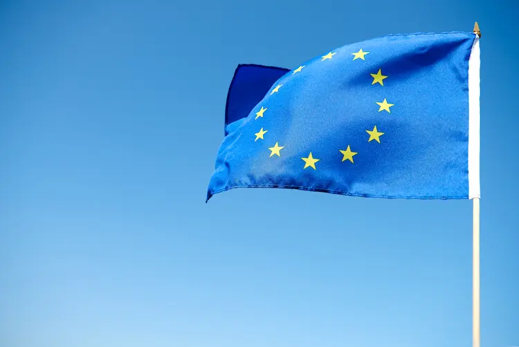 Flaga Unii Europejskiej powiewająca na maszcie na tle błękitnego nieba